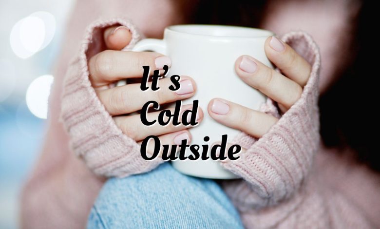 Cozy winter scene with hot cocoa and blanket featuring It’s Cold Outside quotes